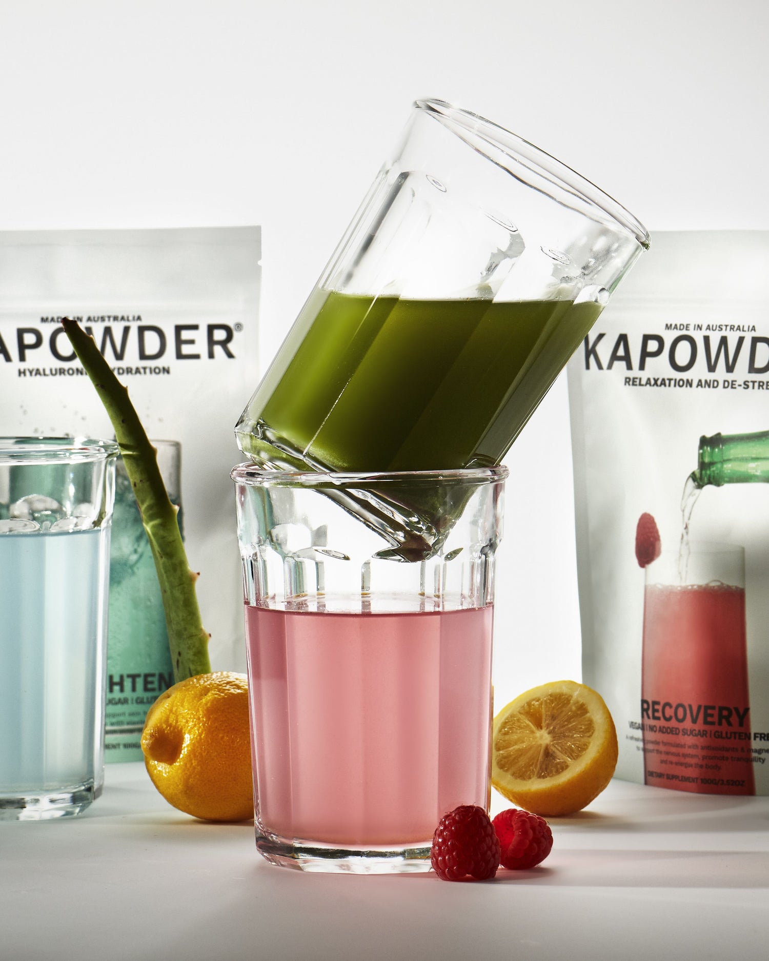 Collection of KAPOWDER products in use including enlighten for hyaluronic hydration, recovery for relaxation and magnesium and vitality greens powder in a glass of water.